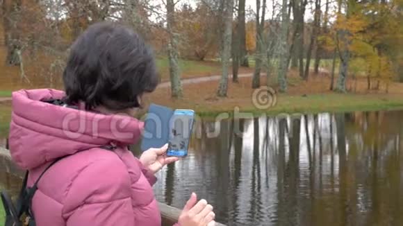 乌云密布的秋日女人在智能手机上拍照鸭子漂浮在池塘里视频的预览图