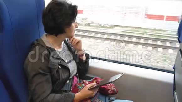 白种人女人坐在火车窗口拿着平板电脑看着窗外支撑着她的下巴视频的预览图