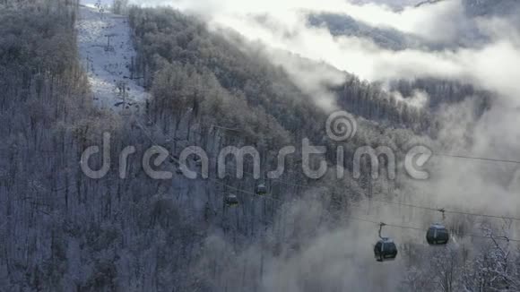 滑雪电梯在低地白色雪山云林上移动提供带滑雪者和滑雪板的滑雪缆车视频的预览图