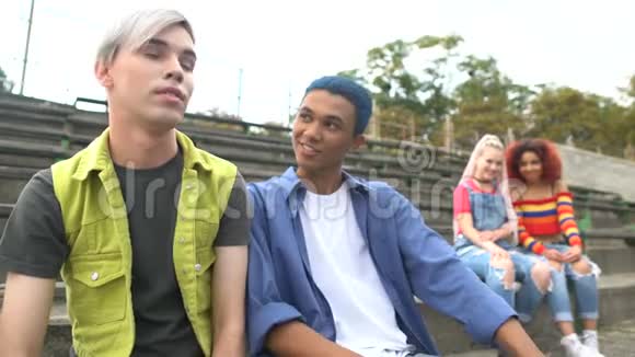 青少年与年轻的女性朋友调情坐在大学体育场的长椅上视频的预览图