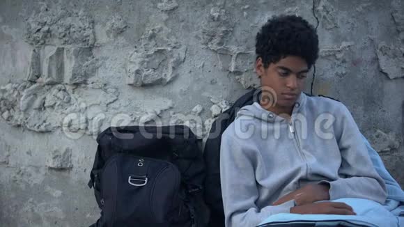 无家可归的男青少年在背包附近的街道上躺着睡袋视频的预览图