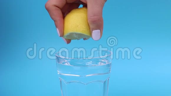女用手在蓝色背景下将柠檬汁挤成一杯水视频的预览图