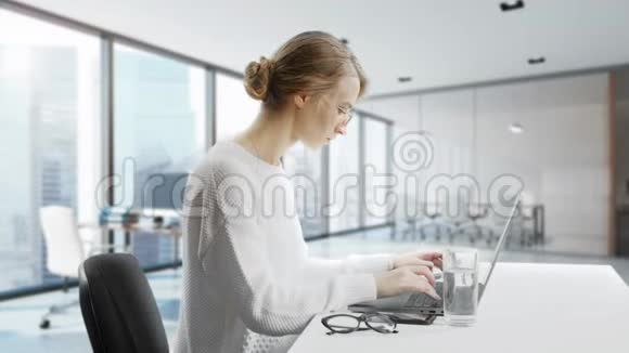 女人坐在办公桌前用笔记本电脑年轻的欧洲女商人正在工作正在喝着一杯来自视频的预览图
