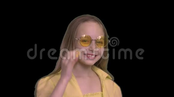 肖像微笑的女孩穿着黄色的裙子戴着黄色的眼镜被隔离在黑色的背景上快乐少女视频的预览图