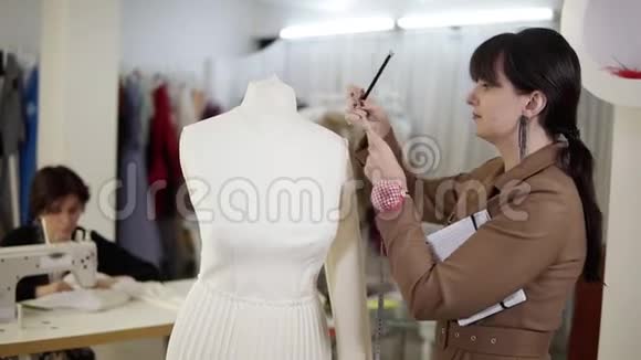一位专业的女裁缝在制作一种新的时装时用测量带在人体模型上采取措施的肖像视频的预览图