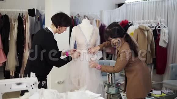 两位女设计师通过独家订购缝纫面料和将细节固定在一件婚纱上创作婚纱的肖像视频的预览图