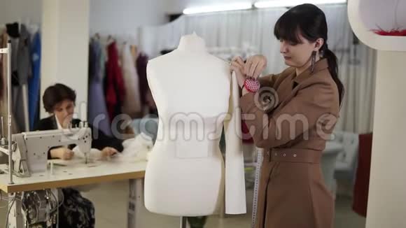 布吕内特的一位女士把一件布套钉在人体模型上另一位女士在缝纫机上工作视频的预览图