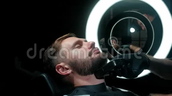 巴伯把客户的胡子剃在椅子上胡子的发型用电动剃须刀刮胡子装饰视频的预览图