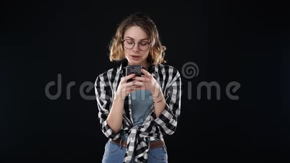 集中的欧洲女性穿休闲服装的肖像格子衬衫和牛仔裤手持智能手机和打字视频的预览图
