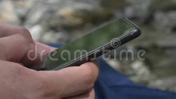 山溪背景下的男性手型智能手机短信视频的预览图