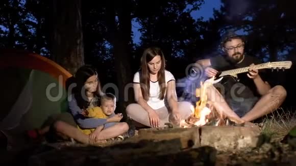 一群朋友带着一个孩子在炉火旁休息一个男人在弹吉他视频的预览图
