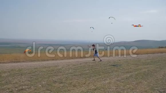 一个男孩带着风筝沿着路跑梦想飞翔孩子们游戏蓝天背景下的男孩视频的预览图