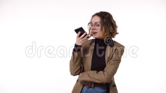 穿着时尚休闲服装和眼镜的漂亮黑发女人在她的手机上记录了一条声音信息视频的预览图