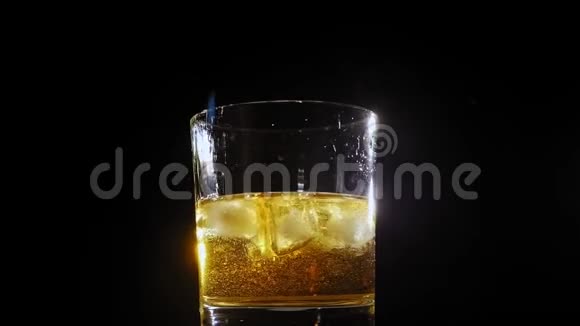 在黑色背景下将冰块倒入一杯威士忌中视频的预览图