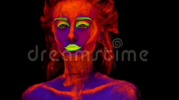 一个年轻漂亮的女孩她的身体上有紫外线涂料看着一个艺术家用画笔的手给她画画视频的预览图