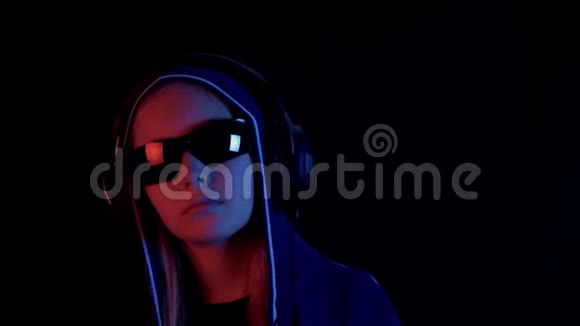 少女在引擎盖和耳机听音乐在黑色工作室与霓虹灯红色和蓝色照明数码朋克女孩视频的预览图
