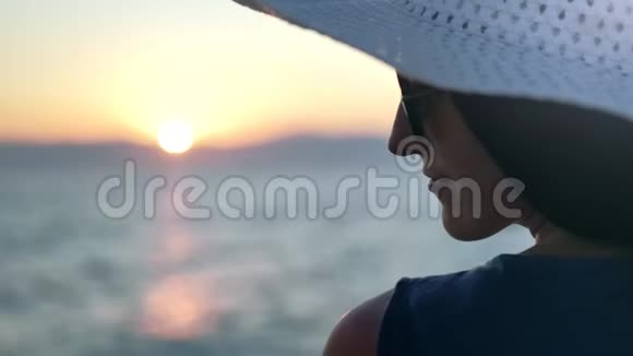 戴着帽子和太阳镜的贴身时尚女士欣赏美丽的日落和海景视频的预览图