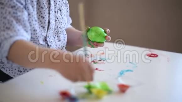 一个小小孩用画笔在桌子上画一个绿色的复活节彩蛋视频的预览图
