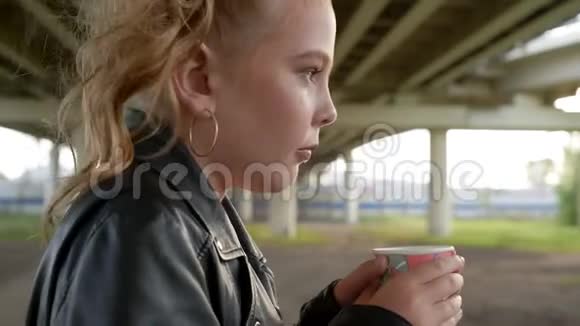 冰冻的朋克女孩手里拿着热饮料在城市街道上取暖穿黑色皮夹克的摇滚女孩视频的预览图