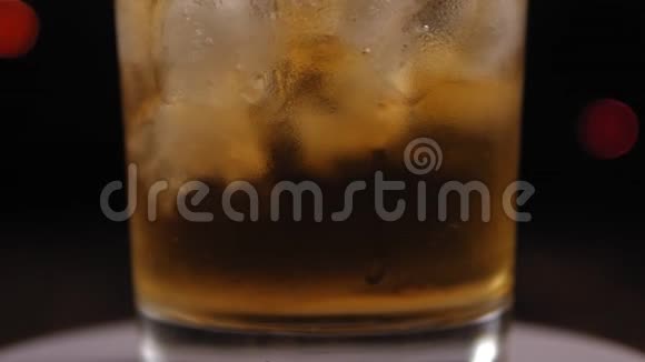 一杯威士忌的特写在闪烁的背景上旋转着冰视频的预览图