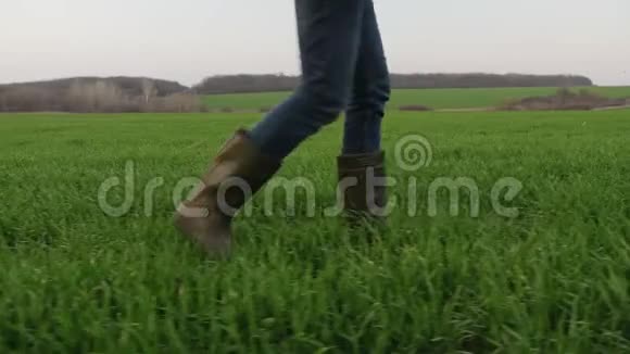 一个穿着橡胶靴的农夫穿过一片绿色的田野视频的预览图
