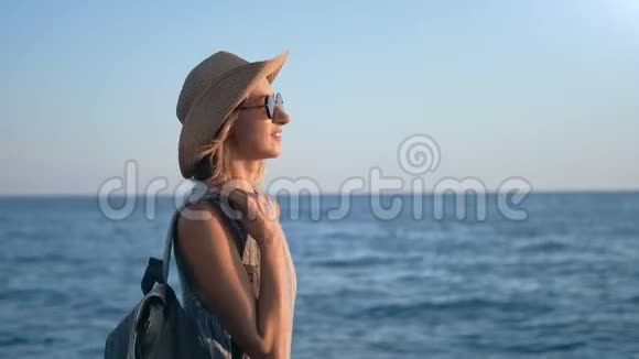 带笑的背包游客女士在海滩上散步在海景的背景下享受日落视频的预览图