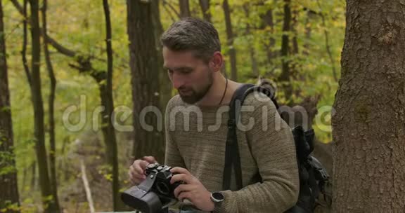 男性白种人游客坐在秋天的森林里拿着相机说话自信的白发帅哥视频的预览图