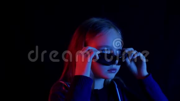 穿着黑色太阳镜的少女在黑暗的房间里看着红蓝光网络垃圾女孩咀嚼肖像视频的预览图