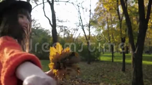 戴着长发帽子的微笑女孩的肖像她牵着朋友的手带着他在秋天的公园散步视频的预览图