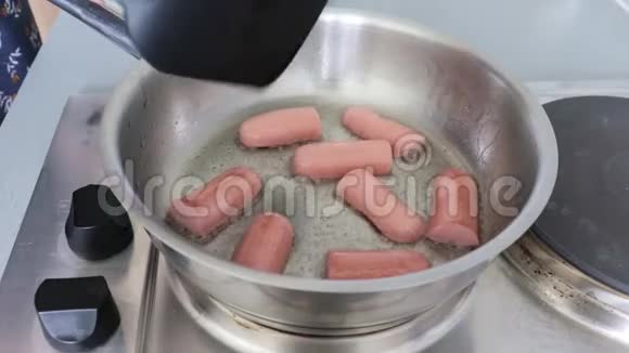 一个女人在家里用电炉把大量的油放在钢锅里手里煎香肠视频的预览图