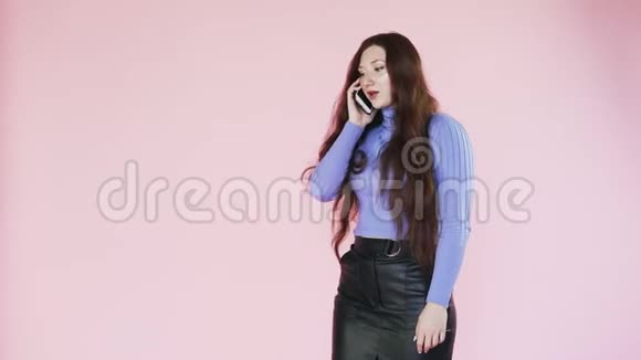 年轻的红发女孩带着牙套在粉红色的背景打电话视频的预览图