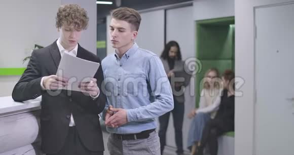 年轻的白种人男人拿着笔记本电脑站在空地上说话办公室工作人员讨论业务视频的预览图