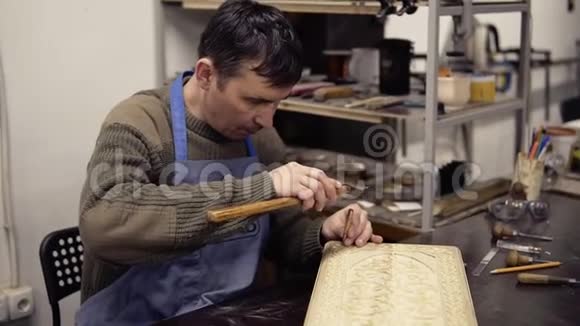 一个穿着蓝色工作服的工匠坐在他工作的地方在后座上雕刻木制装饰品一个男人的肖像视频的预览图