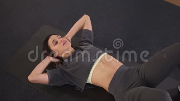 一个穿灰色运动服的欧洲年轻女子独自在健身房的地板上抽腹肌体育和健身视频的预览图