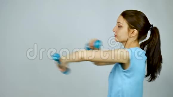 年轻漂亮的运动女性手中有哑铃在灰色工作室背景下做运动一个漂亮的女孩视频的预览图