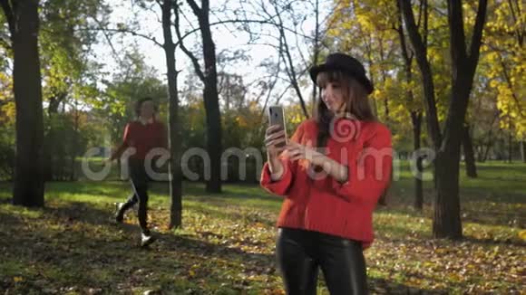 秋天的季节有趣迷人的女孩朋友在公园里的秋叶背景下通过电话拍照散步视频的预览图