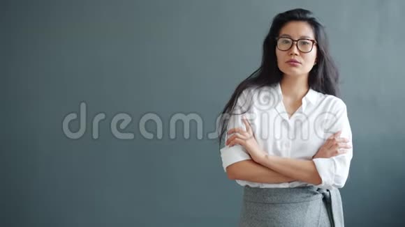 严肃的亚洲女商人站在灰色背景下的慢镜头肖像视频的预览图