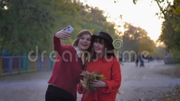 穿着红色衣服的漂亮年轻女性在手机上拍照手里拿着树叶然后把它们扔起来然后拿一个视频的预览图