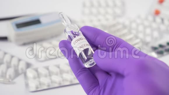 带医疗设备和药片的白色桌子上戴着蓝色防护手套的冠状病毒疫苗安瓿视频的预览图