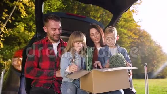 他们的好孩子坐在汽车的后备箱里手里拿着一个绿花的大盒子这让父母感到满意视频的预览图