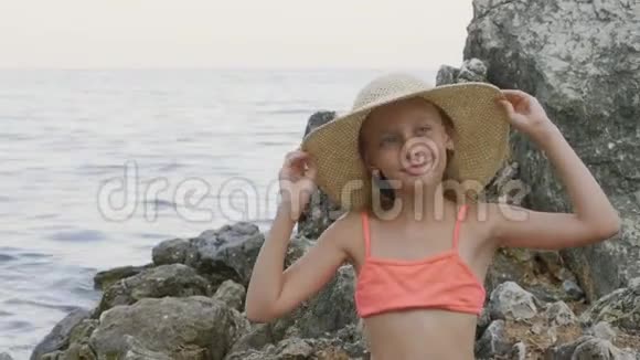 可爱的少年女孩穿比基尼在海水中的石头上戴草帽在海水中戴着夏帽的美女肖像视频的预览图
