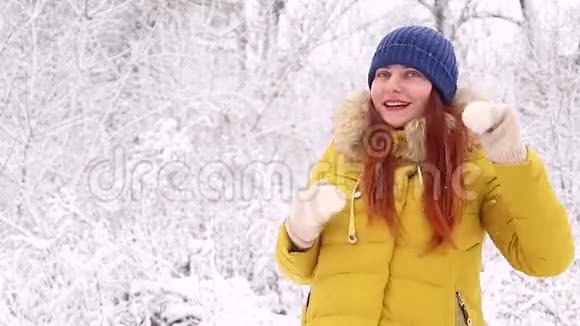 一个年轻的女孩穿着一件温暖的黄色夹克和一顶针织的蓝色帽子在冬季景观的背景下跳舞视频的预览图