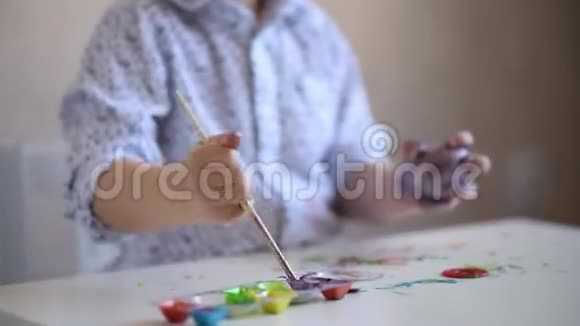 一个小小的孩子用画笔在桌子上涂上紫色的复活节彩蛋视频的预览图