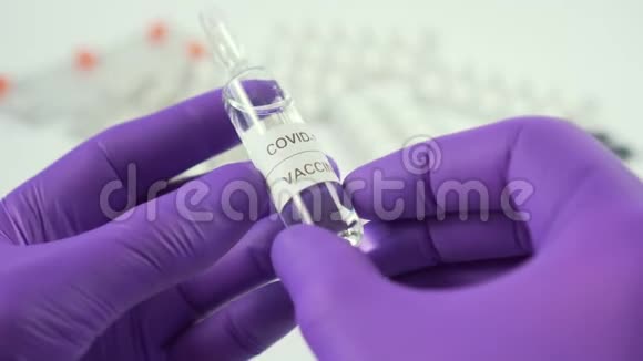 冠状病毒疫苗安瓿双手戴蓝色防护手套放在一张白色桌子上上面医疗药片和胶囊视频的预览图