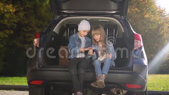 活泼可爱的少年兄妹坐在汽车后备箱里玩电话视频的预览图