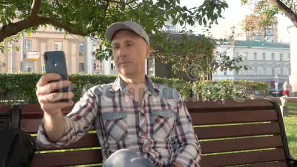 一个白人男人坐在公园里的长椅上自拍视频的预览图
