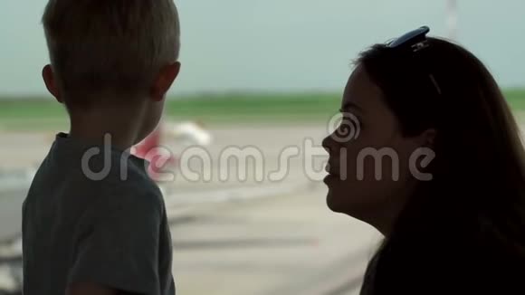 母亲的剪影和儿子站在机场的窗口视频的预览图