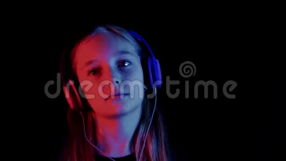 美丽的青少年女孩听音乐耳机在黑暗的房间与霓虹灯照明喜欢音乐的放松女孩视频的预览图