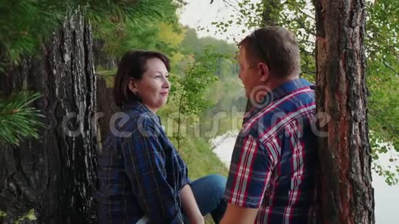 快乐的成年夫妇在松林里的河岸拥抱浪漫的男人和女人在夏天的河边接吻视频的预览图