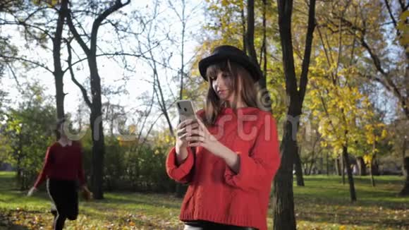 秋天美丽的女孩在公园里玩得很开心在秋天扔树叶在手机上自拍视频的预览图